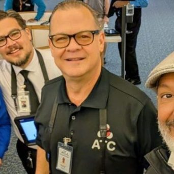 Four men smiling at an airport, three holding tablets with welcome messages.
