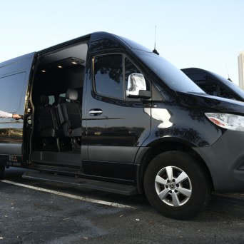 Man in vest opens door of a black van in a parking lot.