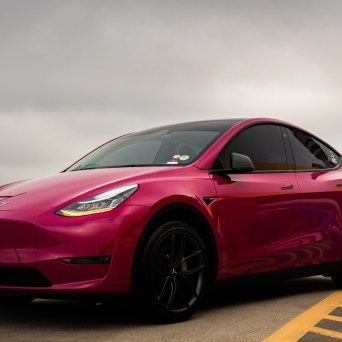 Red electric car parked on a cloudy day in a parking lot.