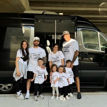 Group of adults and children in matching shirts standing by a black van.